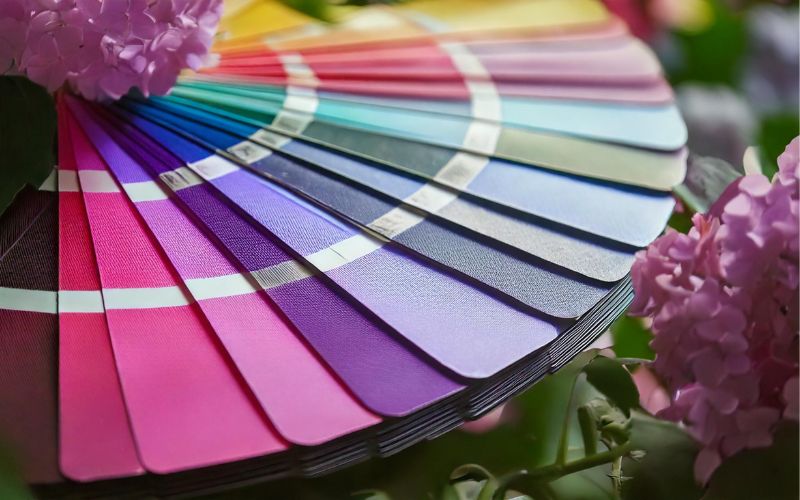 Muestrario con pinturas murales en tonos fuertes y suaves desde rosa hasta azul y verde, rodeado de flores – inspiración para un diseño interior individual.
